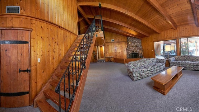 carpeted living room featuring visible vents, wood walls, vaulted ceiling with beams, and stairway