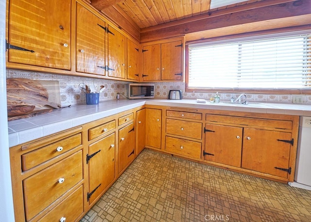 kitchen featuring a sink, stainless steel microwave, white dishwasher, wood ceiling, and tile countertops