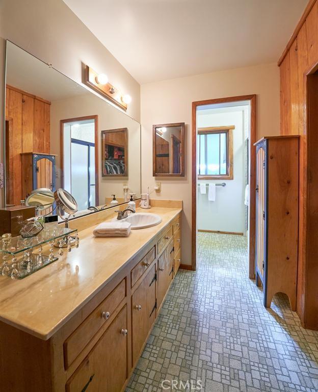 full bathroom featuring a sink, baseboards, double vanity, and brick patterned floor