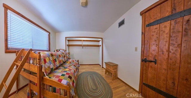 bedroom with light wood-style floors, visible vents, a closet, and lofted ceiling
