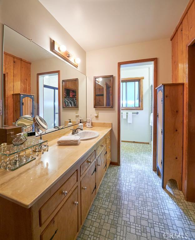 full bath with double vanity, a sink, baseboards, and brick patterned floor