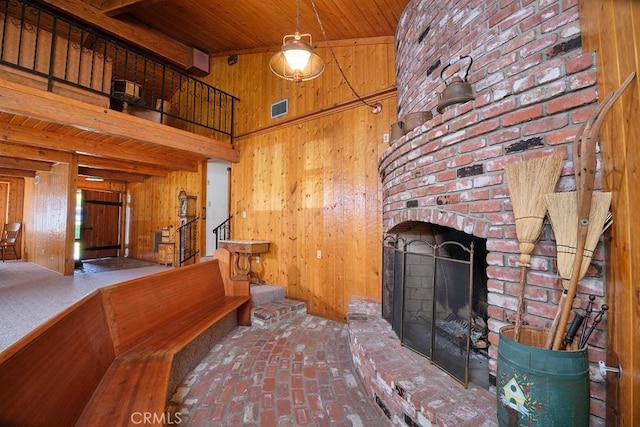 interior space with a towering ceiling, a fireplace, wooden walls, brick floor, and wooden ceiling
