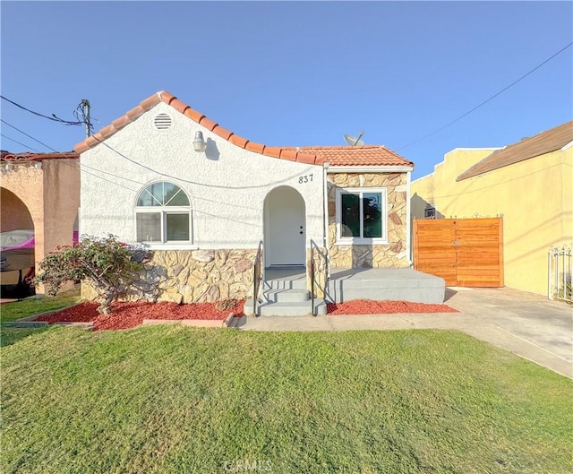 mediterranean / spanish house with stone siding, a tile roof, and a front lawn