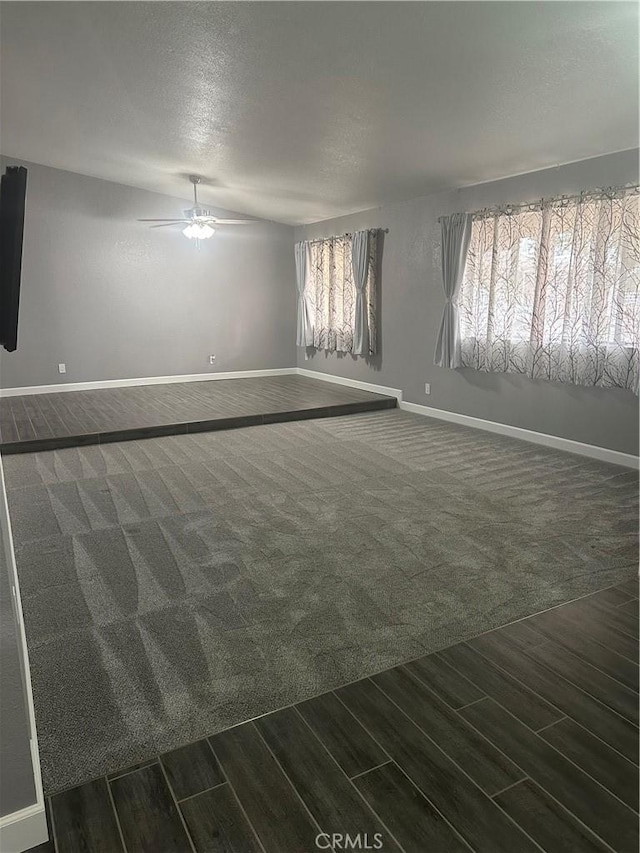 unfurnished room featuring baseboards, dark carpet, a textured ceiling, and wood finish floors