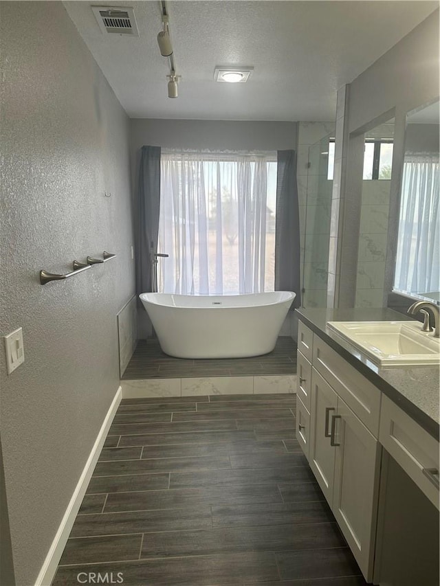 full bath featuring wood tiled floor, visible vents, a freestanding bath, and vanity