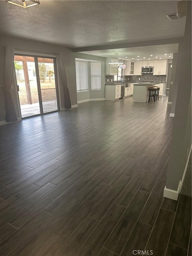 unfurnished living room with dark wood-style floors, visible vents, a textured ceiling, and baseboards