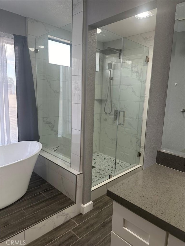 full bathroom with a stall shower, a textured wall, a soaking tub, and wood finish floors