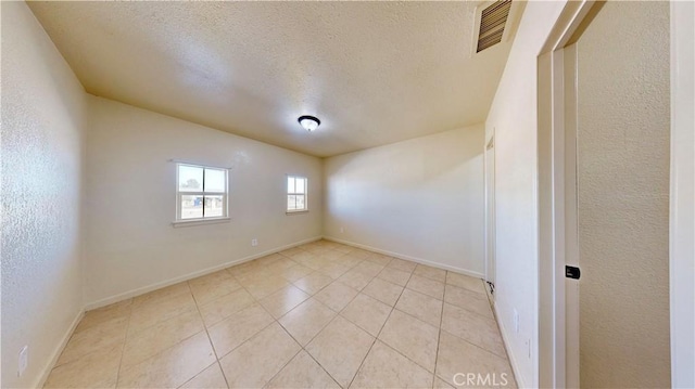 unfurnished room featuring visible vents, a textured wall, light tile patterned flooring, a textured ceiling, and baseboards