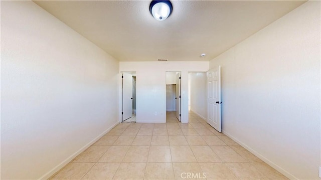 unfurnished bedroom featuring a spacious closet, light tile patterned flooring, visible vents, and baseboards