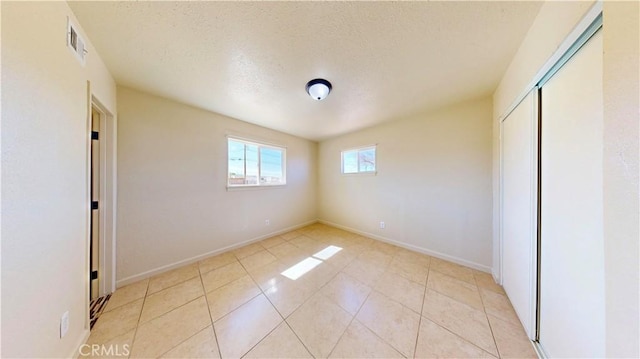 unfurnished bedroom featuring light tile patterned floors, a closet, visible vents, a textured ceiling, and baseboards