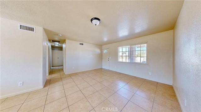 unfurnished room with light tile patterned floors, visible vents, and a textured wall