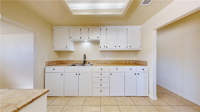 kitchen featuring light tile patterned floors, visible vents, white cabinets, a sink, and baseboards