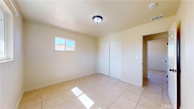 unfurnished bedroom featuring light tile patterned floors, a closet, visible vents, and baseboards