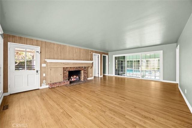 unfurnished living room with a brick fireplace, light wood-type flooring, visible vents, and a healthy amount of sunlight