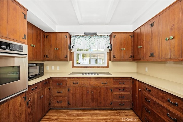 kitchen with brown cabinets, black appliances, light countertops, and light wood-style floors