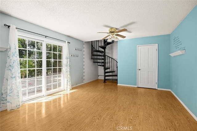 spare room with light wood finished floors, baseboards, stairway, and a textured ceiling