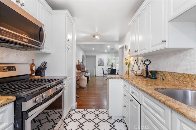 kitchen with light stone countertops, white cabinetry, stainless steel appliances, and backsplash