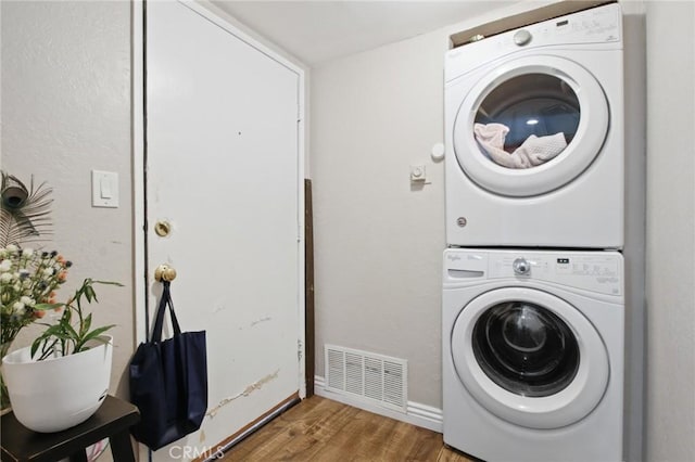 clothes washing area featuring stacked washer and dryer, visible vents, wood finished floors, laundry area, and baseboards