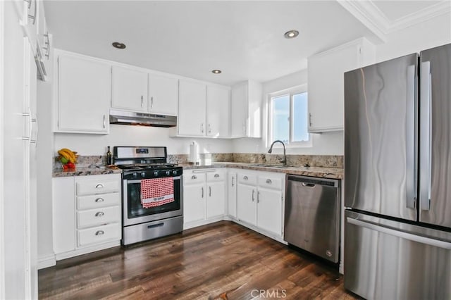 kitchen with dark stone countertops, stainless steel appliances, under cabinet range hood, white cabinetry, and a sink