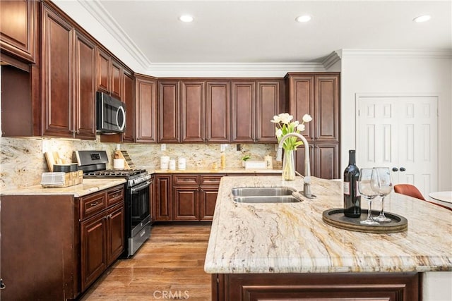 kitchen featuring a center island with sink, stainless steel appliances, crown molding, light wood-type flooring, and a sink