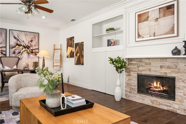 living room with built in shelves, crown molding, visible vents, a stone fireplace, and wood finished floors