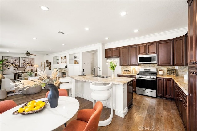 kitchen with stainless steel appliances, a fireplace, a sink, dark wood finished floors, and a center island with sink