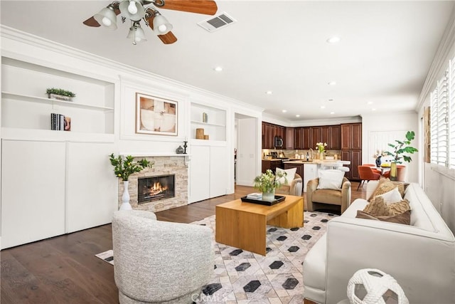 living room featuring visible vents, a ceiling fan, light wood-style flooring, crown molding, and a fireplace