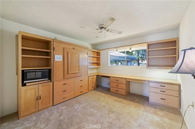 unfurnished office with light colored carpet, built in desk, ceiling fan, and a textured ceiling