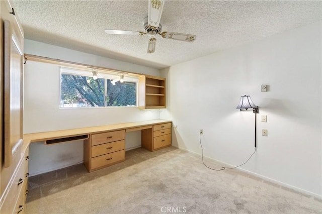 unfurnished office featuring a ceiling fan, built in study area, a textured ceiling, baseboards, and light colored carpet