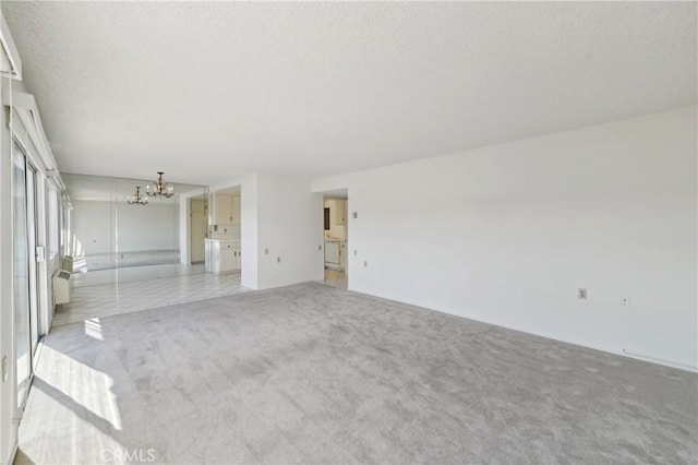 empty room featuring a textured ceiling, an inviting chandelier, and light colored carpet