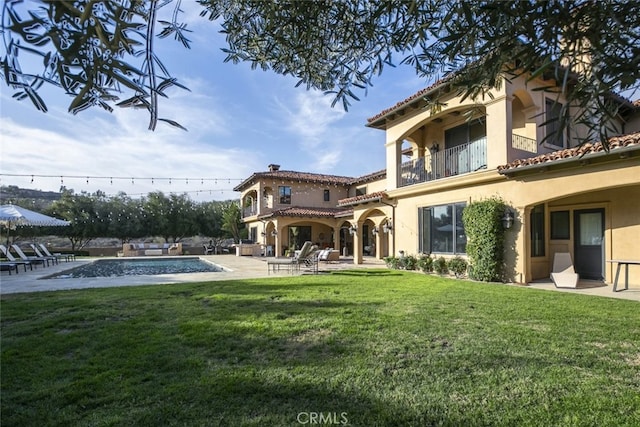 back of property featuring a patio, a balcony, an outdoor pool, a lawn, and stucco siding