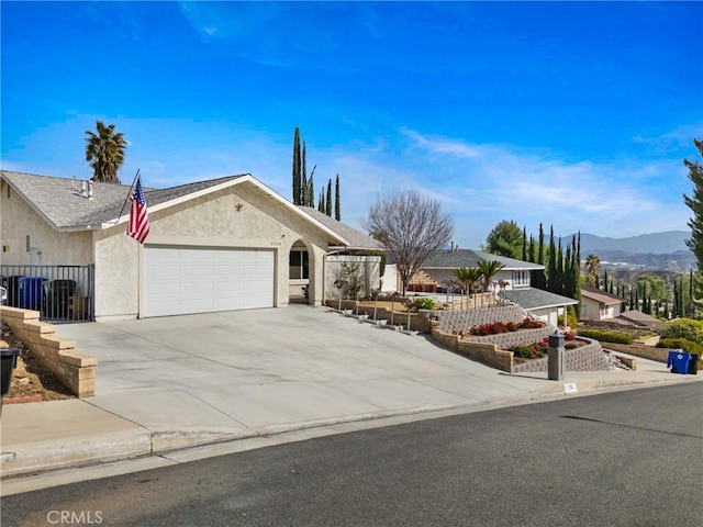 single story home with driveway, an attached garage, fence, a mountain view, and stucco siding