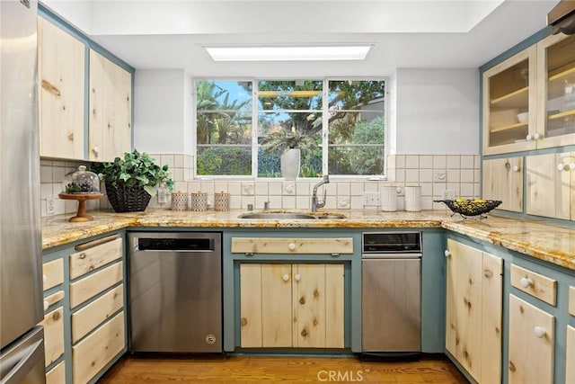 kitchen featuring stainless steel appliances, tasteful backsplash, a sink, and light stone countertops