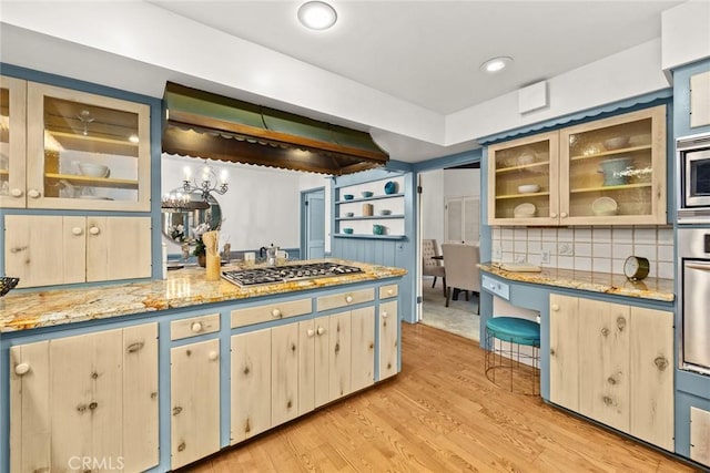 kitchen featuring stainless steel appliances, light wood-type flooring, light stone countertops, tasteful backsplash, and glass insert cabinets