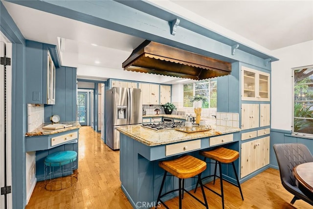 kitchen with light wood finished floors, a breakfast bar area, blue cabinets, light stone countertops, and stainless steel appliances