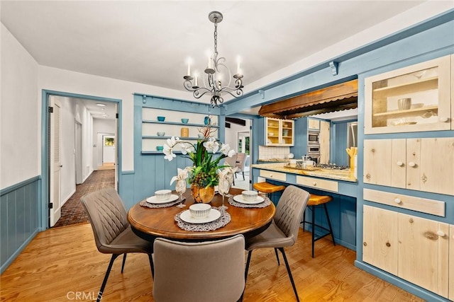 dining space with light wood-type flooring, a wainscoted wall, and a chandelier