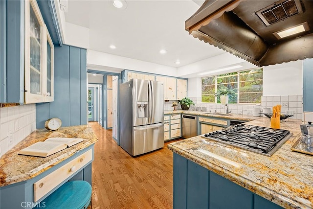 kitchen featuring light wood finished floors, glass insert cabinets, appliances with stainless steel finishes, light stone counters, and blue cabinetry