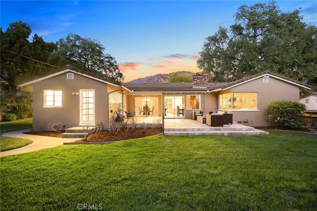 back of property at dusk featuring a lawn, outdoor lounge area, a patio, and stucco siding