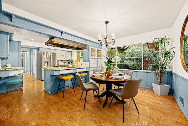 dining area with a wainscoted wall, light wood-style flooring, and a chandelier