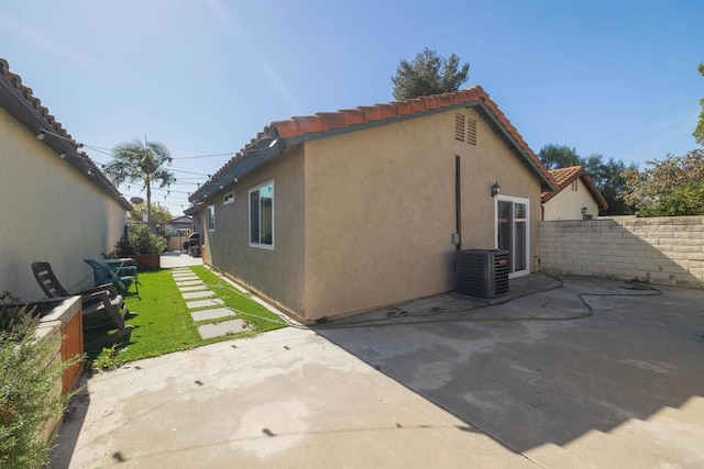 view of side of home featuring a patio, a tiled roof, fence, central air condition unit, and stucco siding