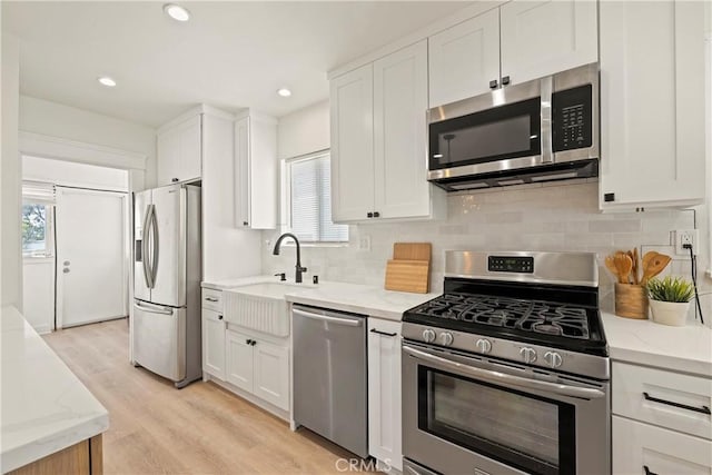 kitchen with white cabinets, decorative backsplash, light stone counters, stainless steel appliances, and a sink