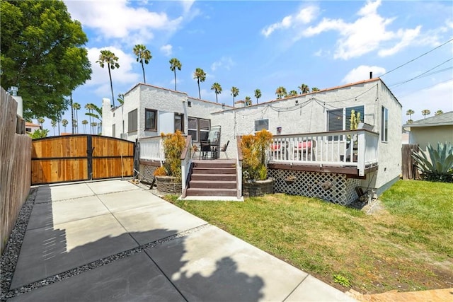 rear view of house with a gate, a yard, a deck, and fence