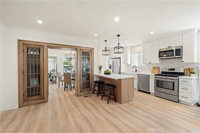 kitchen featuring white cabinets, a breakfast bar area, stainless steel appliances, light countertops, and pendant lighting