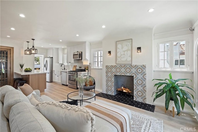 living area with baseboards, light wood-type flooring, a tiled fireplace, and recessed lighting