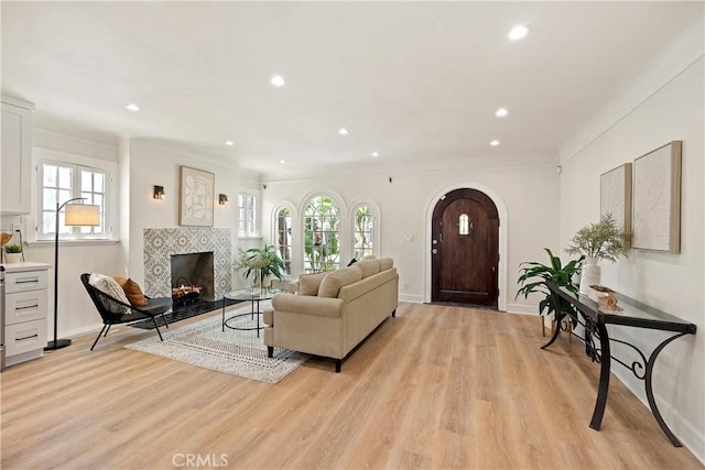 living room featuring arched walkways, recessed lighting, light wood-style floors, a tile fireplace, and baseboards