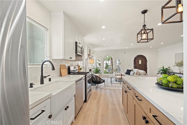 kitchen featuring stainless steel appliances, hanging light fixtures, open floor plan, white cabinets, and light stone countertops