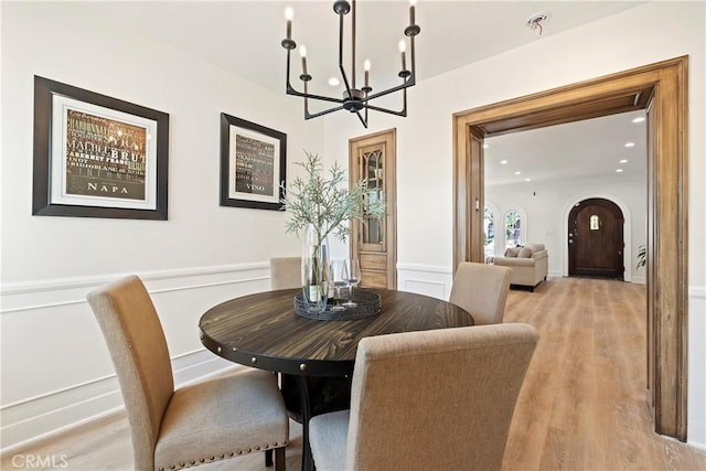 dining space featuring arched walkways, a decorative wall, light wood-style flooring, an inviting chandelier, and wainscoting