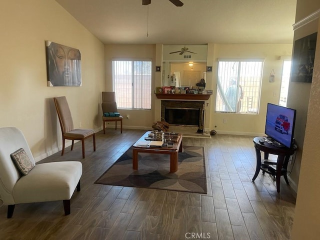 living room featuring baseboards, vaulted ceiling, wood finished floors, and a glass covered fireplace