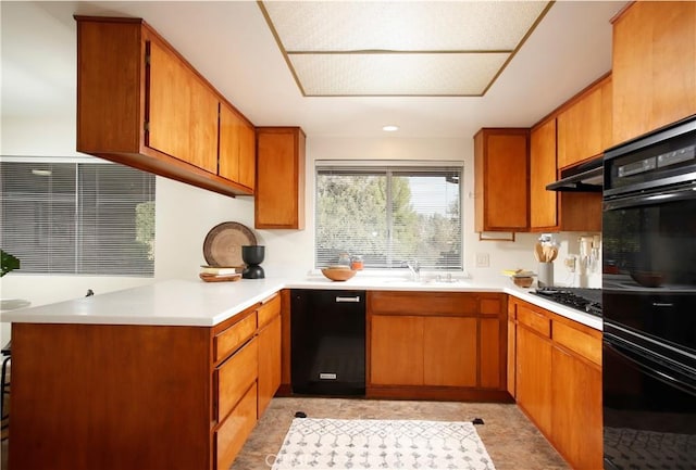 kitchen with light countertops, black appliances, under cabinet range hood, and brown cabinets