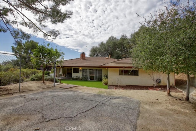 back of house with fence, a tile roof, a lawn, stucco siding, and a chimney